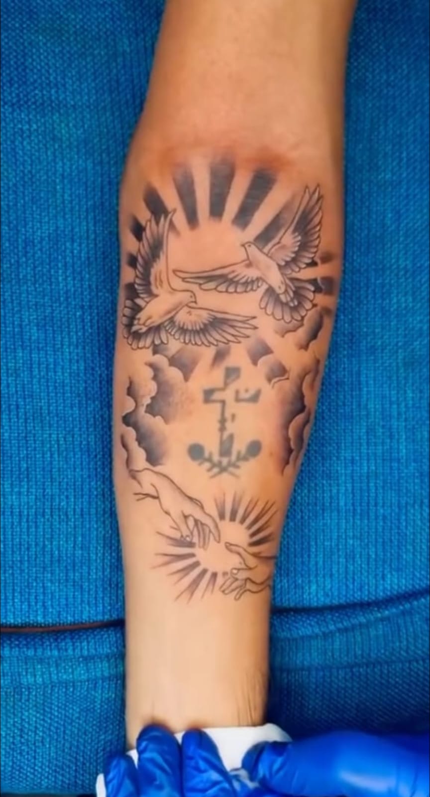 Traditional style tattoo of doves, clouds and a cross on the forearm